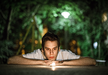 man gazing at candle with trees in background, meditation style