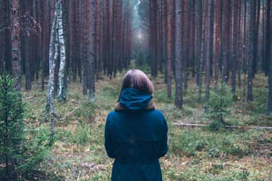 woman in blue coat looking back through the woods, backing up with eft